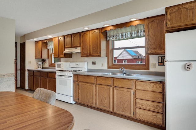 kitchen with under cabinet range hood, light countertops, brown cabinets, white appliances, and a sink