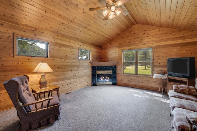 carpeted living room featuring wooden walls, a premium fireplace, ceiling fan, vaulted ceiling, and wooden ceiling