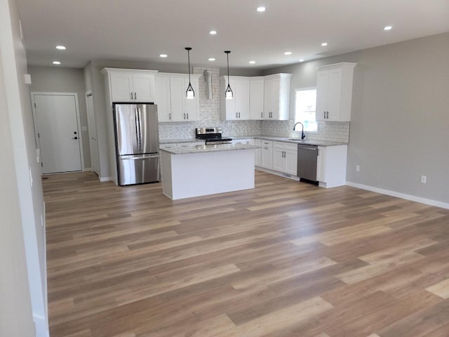 kitchen with light wood-type flooring, appliances with stainless steel finishes, a kitchen island, and white cabinetry