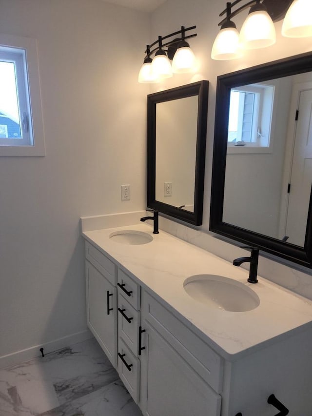 bathroom with marble finish floor, double vanity, a sink, and baseboards