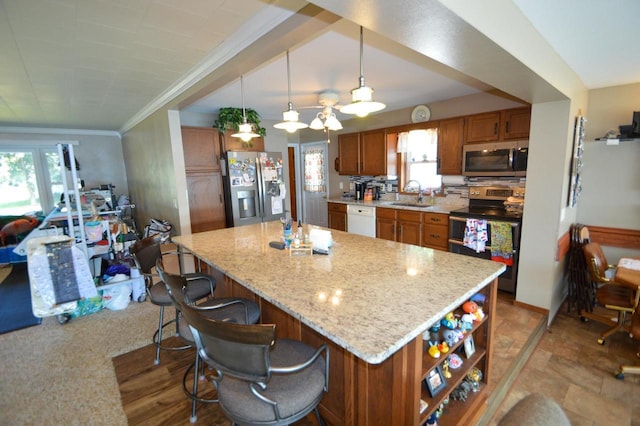 kitchen featuring stainless steel appliances, brown cabinetry, a sink, and pendant lighting