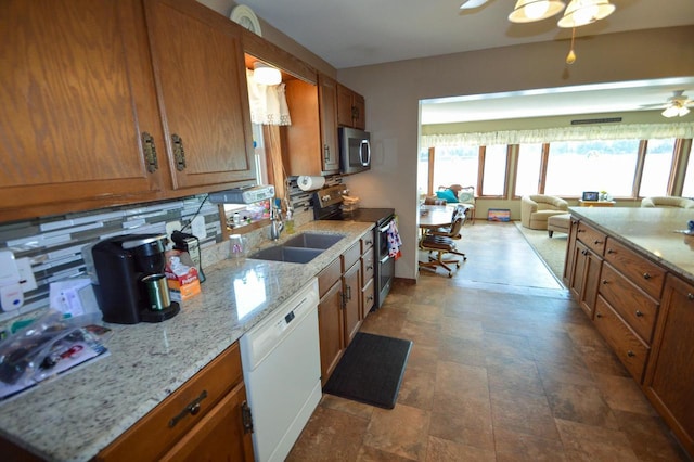 kitchen with brown cabinetry, ceiling fan, open floor plan, stainless steel appliances, and a sink