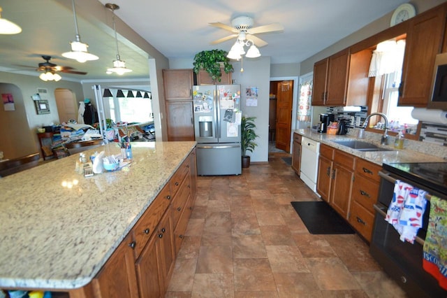 kitchen featuring arched walkways, brown cabinetry, a kitchen island, appliances with stainless steel finishes, and a sink