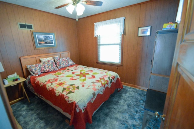 bedroom with wood walls, visible vents, dark colored carpet, and a ceiling fan