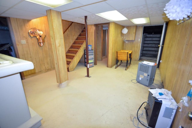 finished basement with wooden walls, a paneled ceiling, and stairway