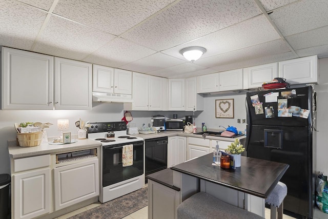 kitchen with a drop ceiling, white cabinets, a kitchen bar, light tile patterned floors, and black appliances