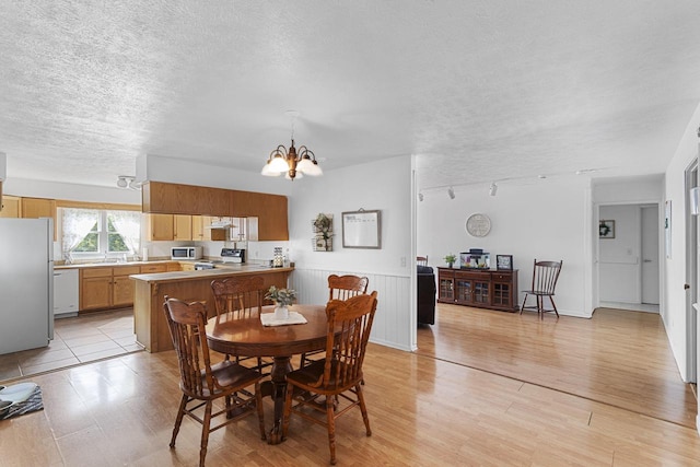 dining area featuring light wood-type flooring, an inviting chandelier, and a textured ceiling