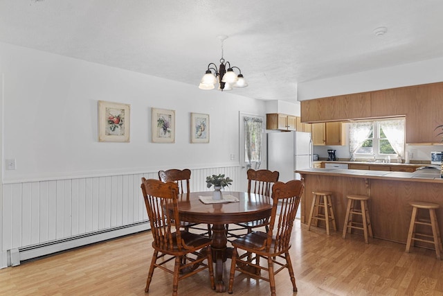 dining area with a notable chandelier, a baseboard heating unit, and light wood-type flooring