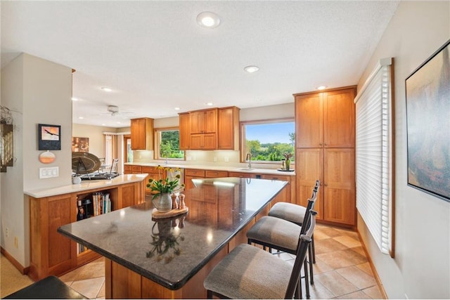 kitchen with sink, a breakfast bar area, a center island, light tile patterned floors, and dark stone counters