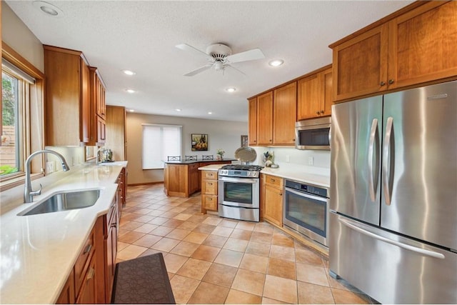 kitchen with sink, light tile patterned floors, appliances with stainless steel finishes, kitchen peninsula, and ceiling fan