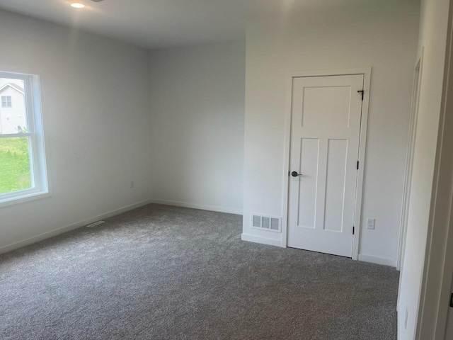 empty room with dark colored carpet, visible vents, and baseboards