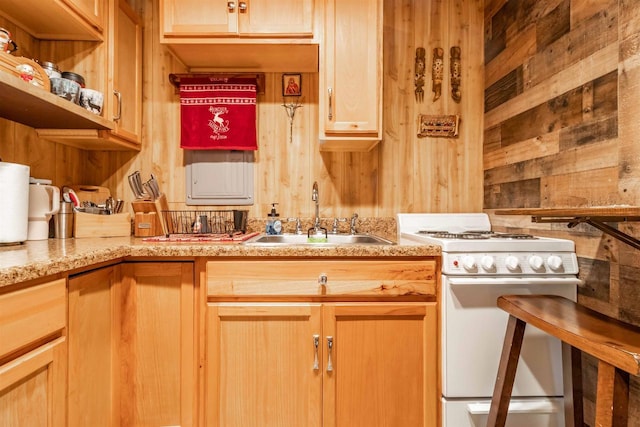 kitchen with light stone countertops, a sink, wood walls, and white gas range