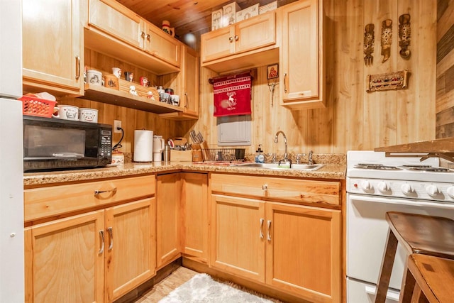 kitchen with light stone counters, white gas range, wood walls, black microwave, and a sink