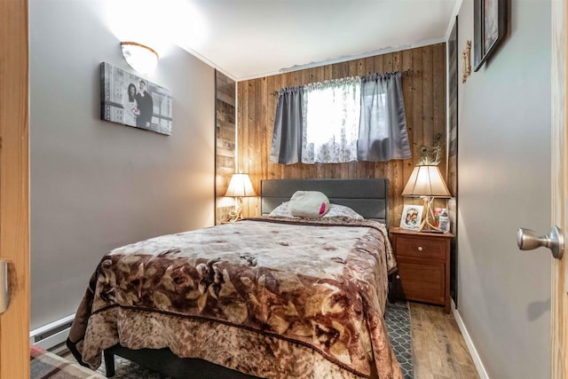 bedroom featuring wood walls, light wood-style flooring, baseboards, and a baseboard heating unit