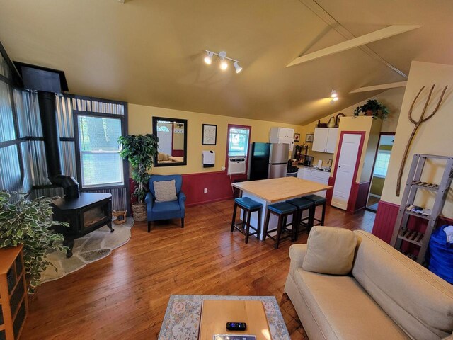 living room with rail lighting, wood-type flooring, a wood stove, and lofted ceiling