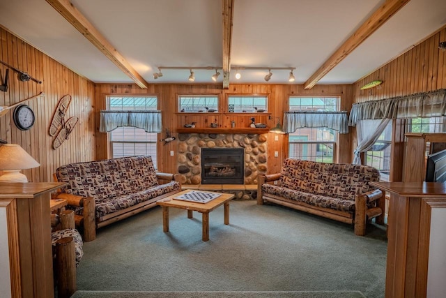 carpeted living room featuring rail lighting, beam ceiling, wood walls, and a stone fireplace