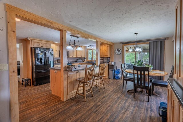 kitchen featuring an inviting chandelier, dark hardwood / wood-style floors, a textured ceiling, black fridge, and a breakfast bar area