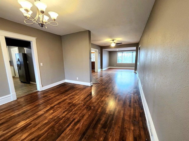 empty room featuring a textured wall, baseboards, wood finished floors, and ceiling fan with notable chandelier