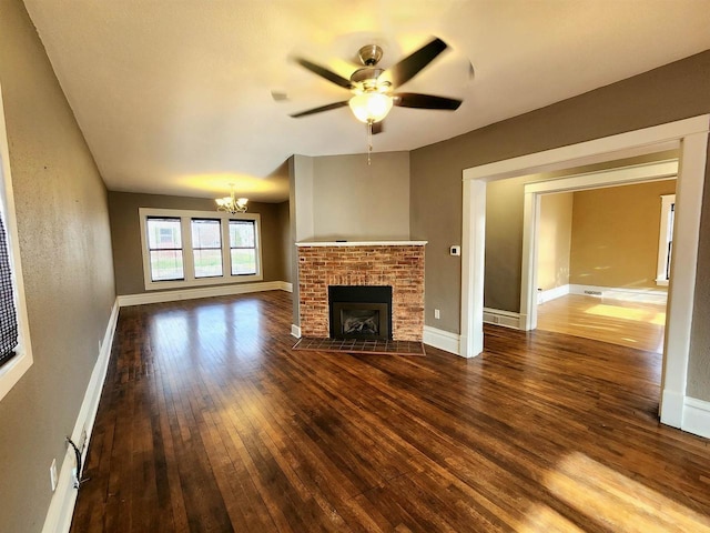 unfurnished living room with baseboards, wood-type flooring, a brick fireplace, and ceiling fan with notable chandelier