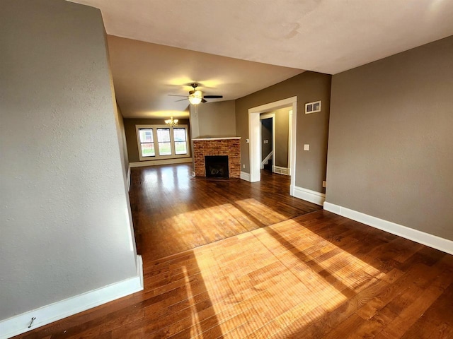 unfurnished living room featuring visible vents, hardwood / wood-style floors, baseboards, a brick fireplace, and ceiling fan