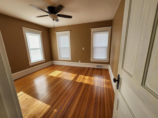 empty room featuring hardwood / wood-style flooring, baseboards, visible vents, and ceiling fan