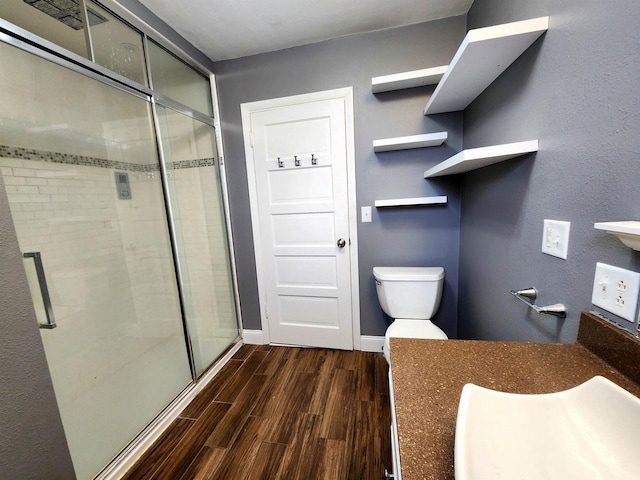 bathroom with baseboards, wood tiled floor, a sink, a shower stall, and toilet