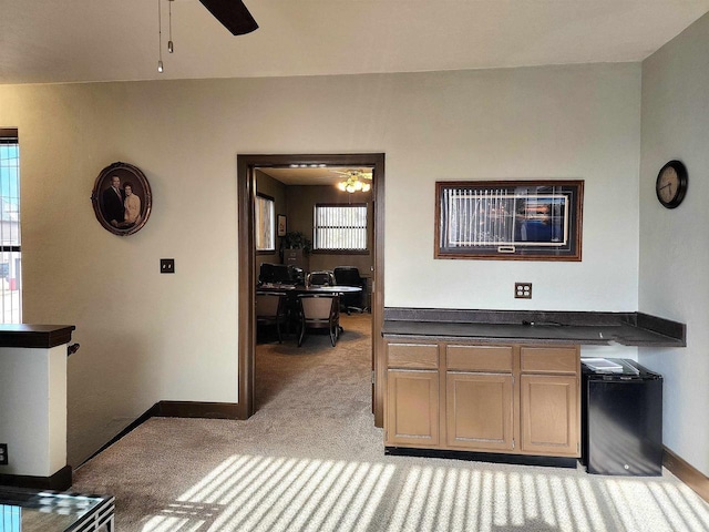 interior space with baseboards, dark countertops, light carpet, and a ceiling fan