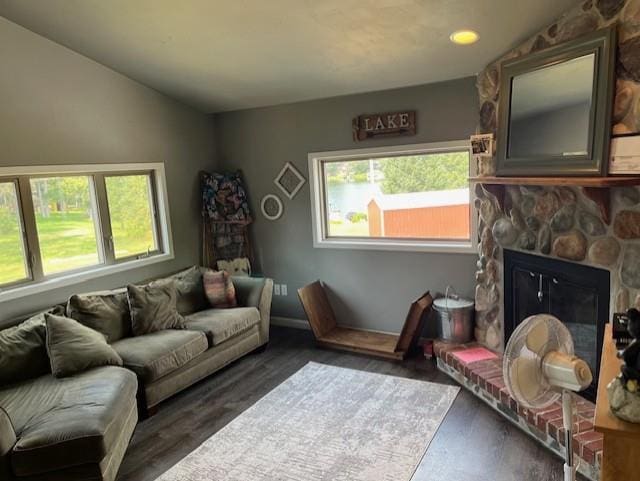 living room with dark hardwood / wood-style floors, vaulted ceiling, and a stone fireplace