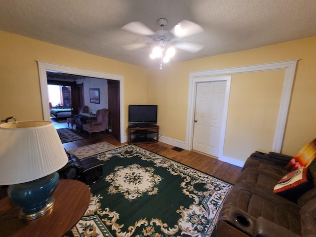 living room featuring ceiling fan, hardwood / wood-style flooring, and a textured ceiling