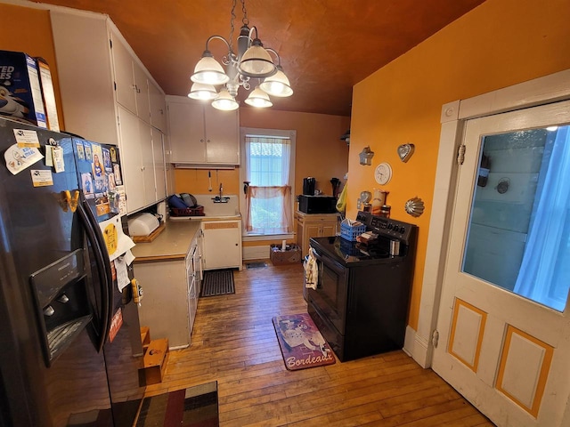 kitchen with decorative light fixtures, a chandelier, white cabinetry, black appliances, and hardwood / wood-style flooring