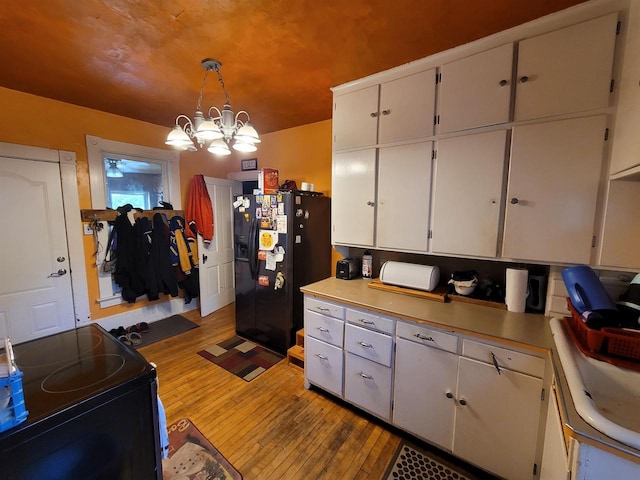 kitchen with black appliances, light wood-type flooring, pendant lighting, white cabinets, and a notable chandelier