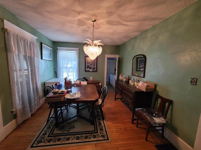 dining space featuring hardwood / wood-style flooring, a notable chandelier, and a textured ceiling