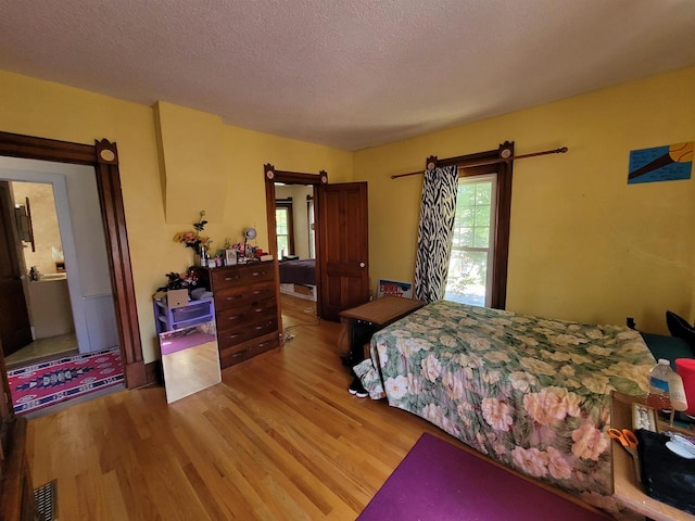 bedroom with a textured ceiling, light hardwood / wood-style flooring, ensuite bath, and a barn door