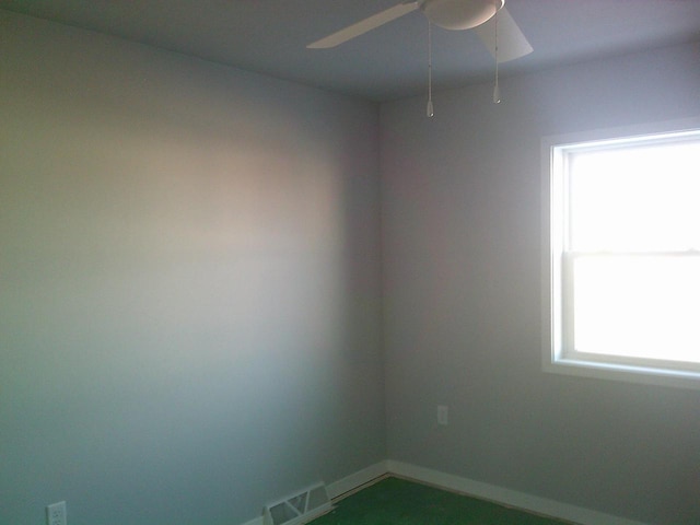 empty room featuring a ceiling fan, visible vents, and baseboards