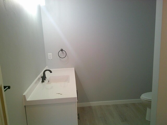 bathroom with toilet, wood finished floors, vanity, and baseboards