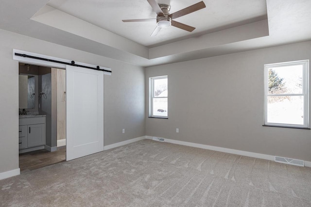 unfurnished bedroom with a tray ceiling, visible vents, a barn door, light carpet, and baseboards