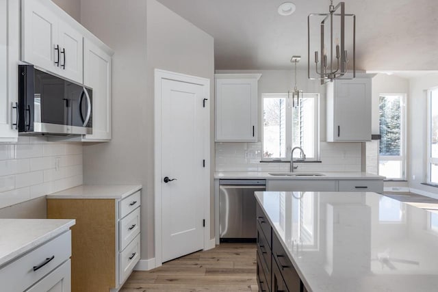 kitchen featuring light wood finished floors, appliances with stainless steel finishes, white cabinetry, pendant lighting, and a sink