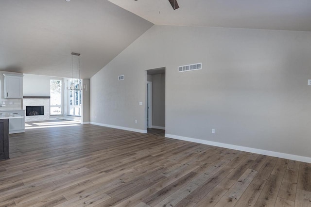 unfurnished living room featuring high vaulted ceiling, light wood-style flooring, visible vents, and ceiling fan with notable chandelier