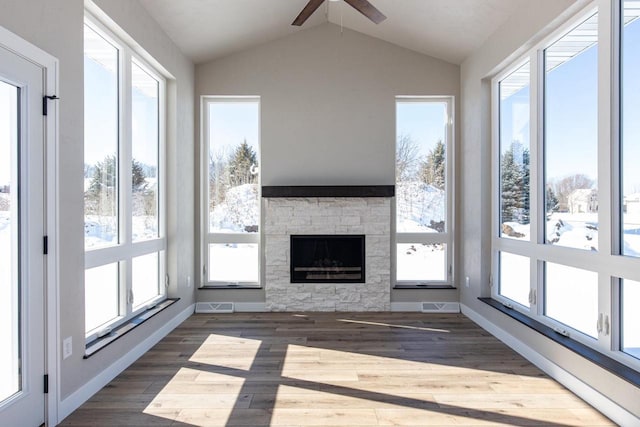 unfurnished sunroom featuring vaulted ceiling, ceiling fan, a stone fireplace, and visible vents