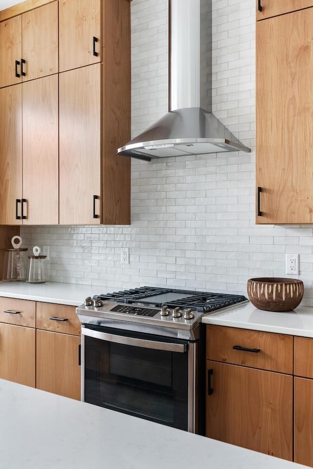 kitchen featuring decorative backsplash, light countertops, wall chimney range hood, and stainless steel gas range oven