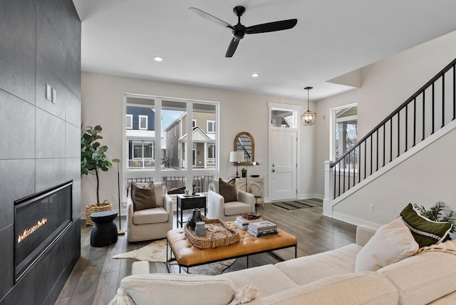 living room featuring a tiled fireplace, stairway, baseboards, and hardwood / wood-style floors