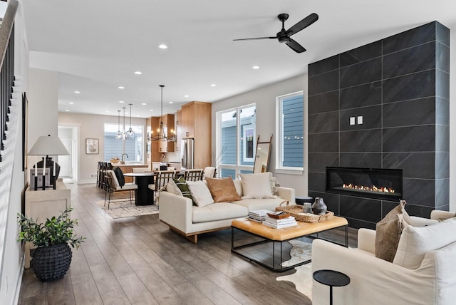 living area with ceiling fan with notable chandelier, recessed lighting, a fireplace, and wood-type flooring