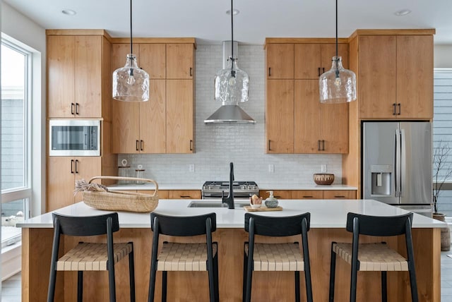 kitchen featuring a center island with sink, hanging light fixtures, light countertops, appliances with stainless steel finishes, and backsplash