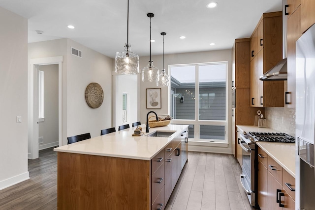 kitchen featuring tasteful backsplash, visible vents, light wood-style floors, stainless steel gas range, and a sink