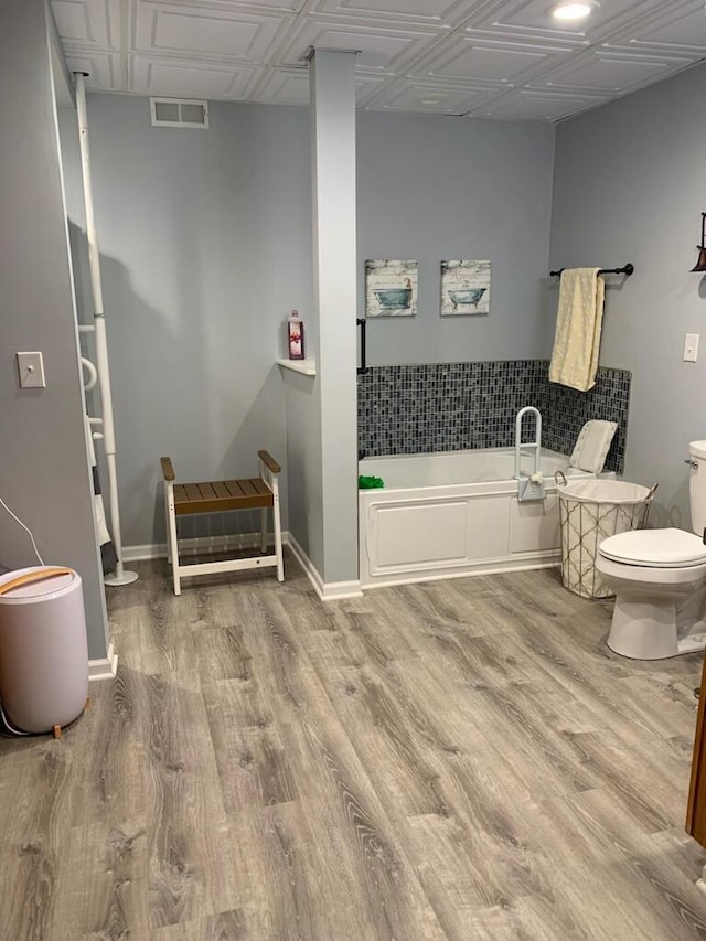 bathroom with a drop ceiling, toilet, hardwood / wood-style flooring, and a bathtub