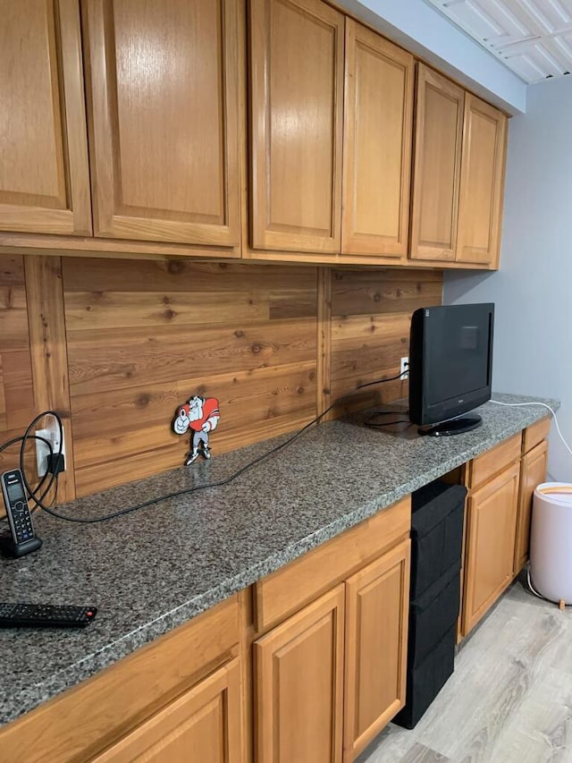 kitchen with built in desk, light wood-type flooring, dark stone counters, and wooden walls