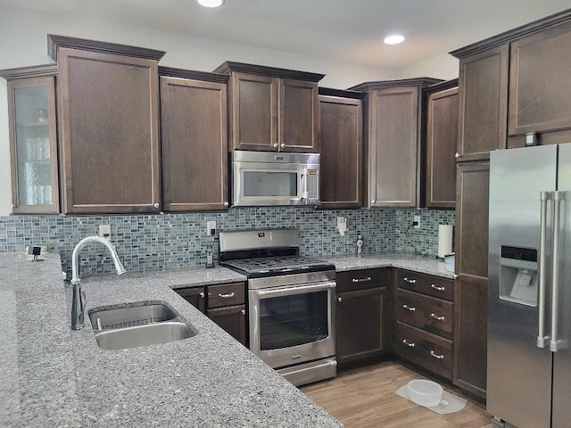 kitchen with light stone counters, stainless steel appliances, light hardwood / wood-style floors, sink, and tasteful backsplash