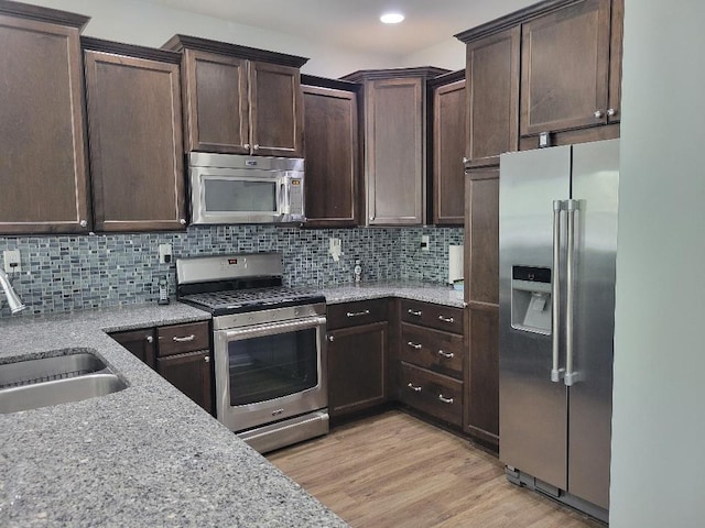 kitchen featuring light wood-type flooring, appliances with stainless steel finishes, light stone countertops, and decorative backsplash