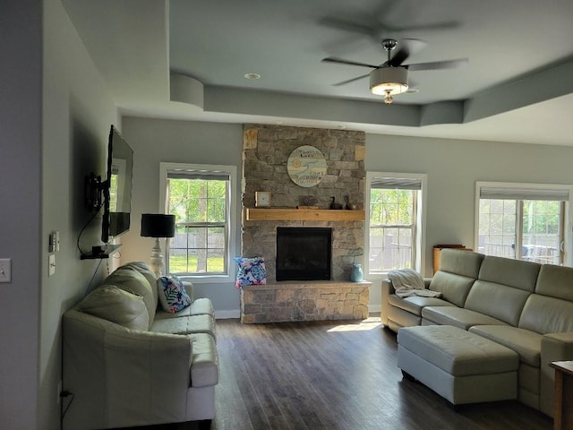 living room featuring ceiling fan, dark hardwood / wood-style floors, a stone fireplace, and a tray ceiling