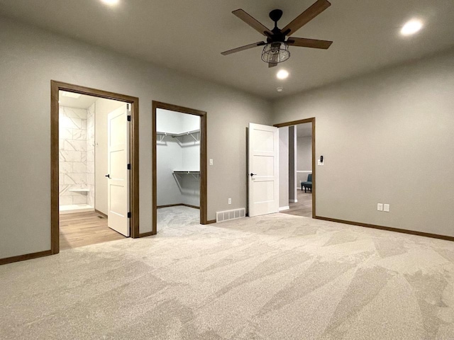 unfurnished bedroom featuring light carpet, a walk in closet, ceiling fan, connected bathroom, and a closet